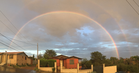 A double rainbow arches over suburban houses against a cloudy sky.